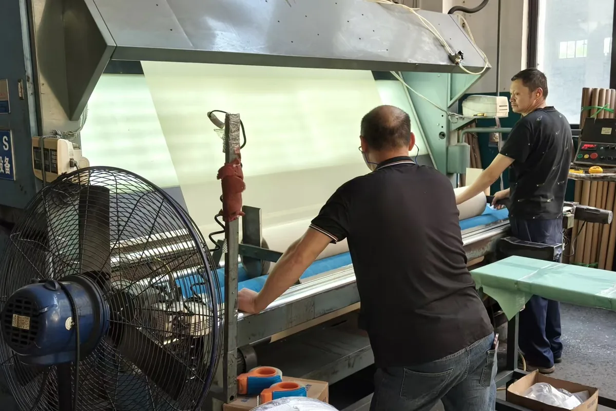 Quality control at the woven vinyl production base in Zhejiang: the fabric checked across the lighted table before packing